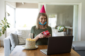 Woman holding a gift box having a video chat on laptop at home