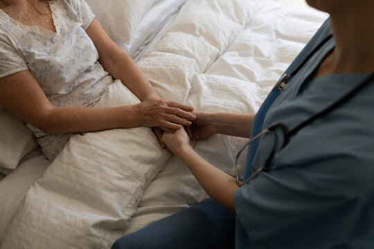 Mid section of Female health worker holding hands of senior woman at home