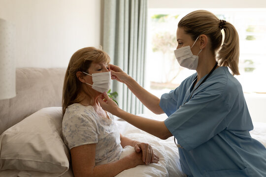  Female health worker putting on face mask on senior woman at home