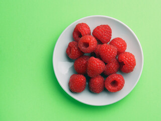 Raspberry berries on a white plate on a green background