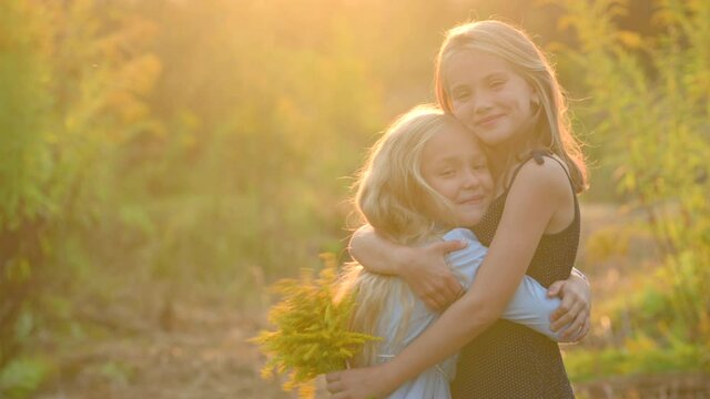 Two happy girls are playing and hugging in the park at sunset. happy family kid and sister lifestyle. couple of happy children