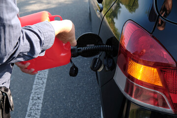 Pouring gasoline from a canister into the car's tank.