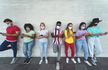 Obraz na płótnie Canvas Young people wearing face mask using mobile smartphone outdoor - Multiracial friends having fun with new technology social media app during corona virus outbreak - Youth millennial lifestyle concept