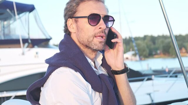 Handsome successful man on the yacht talking on mobile phone. Portrait of business man on sailing boat at sunset.