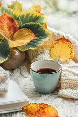Autumn morning coffee. A cup of coffee on a warm sweater against a background of autumn leaves. Light blurred background. Still life concept. Copy space.