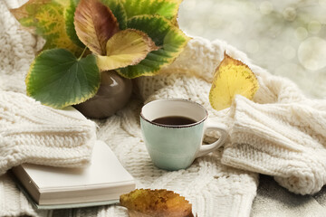 Autumn morning coffee. A cup of coffee on a warm sweater against a background of autumn leaves. Light blurred background. Still life concept. Copy space.