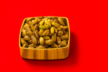 Fresh,crispy pistachio nuts in wooden bowl on vivid red color surface with copy space
