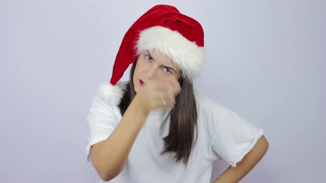 Be careful. Strict and serious young beautiful woman wearing Santa Claus hat over isolated white background warning, making piling hand gesture, scolding