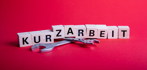 wooden blocks with german word for short time work, Kurzarbeit, above of two wrenches
