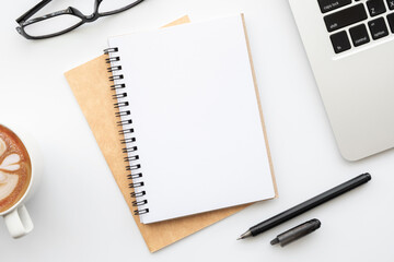 Blank notebook with pen are on top of white office desk table with laptop computer, top view with copy space. Work at home concept.