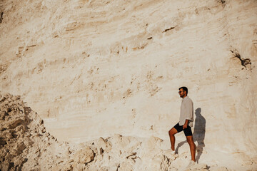 Young stylish bearded man standing on the white stones looking into the horizon. Travel man looks into the distance from the mountain. Mountains peaks and steep cliffs. 