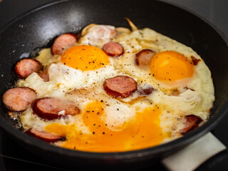 Breakfast - scrambled eggs with sausages and  vegetables in frying pan
