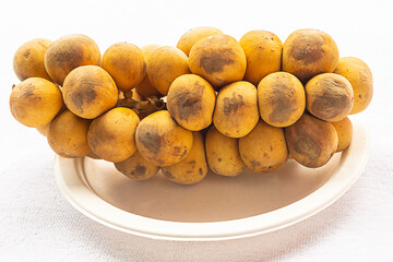 branch of ripe and fresh longkong yellow round on a white plate close-up