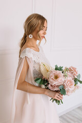 young woman in white wedding dress with long hair before the engagement ceremony with a bouquet of flowers on a white background with a model appearance roses blue eyes