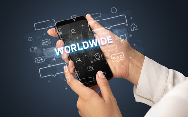 Female hand typing on smartphone with WORLDWIDE inscription, social media concept
