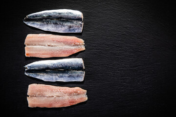 Fresh raw herrings with herbs served on black stone 