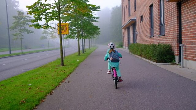 The girl rides the bicycle to school on a foggy morning.