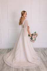 young woman in a white wedding dress with long hair before the engagement ceremony with a bouquet of flowers on a white background with a model appearance important wife for the bride
