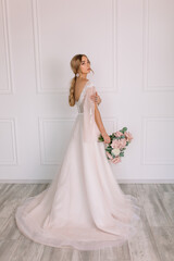 young woman in a white wedding dress with long hair before the engagement ceremony with a bouquet of flowers on a white background with a model appearance important wife for the bride
