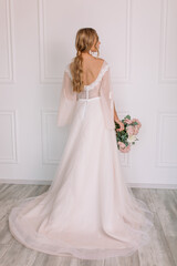 young woman in a white wedding dress with long hair before the engagement ceremony with a bouquet of flowers on a white background with a model appearance important wife for the bride
