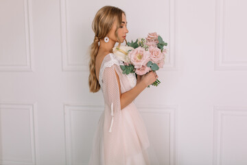 young woman in a white wedding dress with long hair before the engagement ceremony with a bouquet of flowers on a white background with a model appearance important wife for the bride
