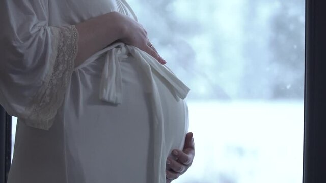pregnant woman stands near the window and looks at photos