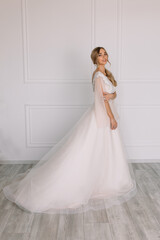 young woman in a white wedding dress with long hair before the engagement ceremony on a white background with a model appearance important wife for the bride posing in front of the photographer
