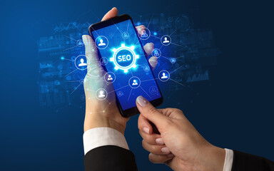 Female hand holding smartphone with SEO abbreviation, modern technology concept
