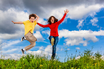 Girl and boy running, jumping against blue sky
