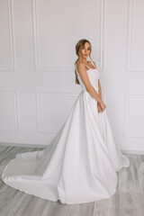 Fototapeta premium young woman in a white wedding dress with long hair before the engagement ceremony on a white background with a model appearance important wife for the bride posing in front of the photographer 