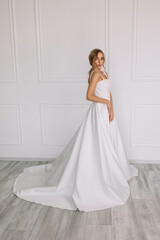 young woman in a white wedding dress with long hair before the engagement ceremony on a white background with a model appearance important wife for the bride posing in front of the photographer
