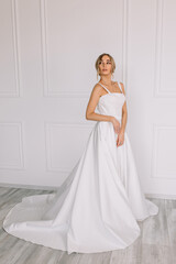 young woman in a white wedding dress with long hair before the engagement ceremony on a white background with a model appearance important wife for the bride posing in front of the photographer
