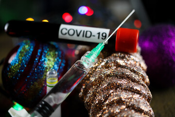 Christmas eve wish list vaccination concept: view on covid-19 blood sample tube, injection syringe needle, medicine vial with shiny decoration (focus on center)