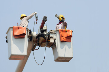 Electricians work together on the electric cable car and electric pole. To maintain the high and low voltage distribution system. They wear a helmet with PPE protection and copy space for your text.