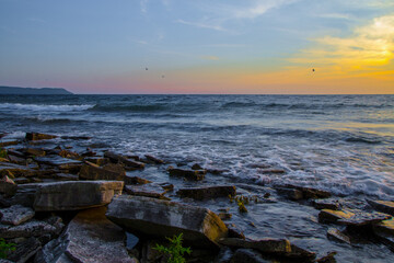Obraz premium Romantic remote twilight beach with waves crashing on the rocky shore on the Great Lakes of Michigan.