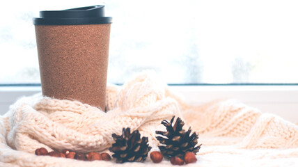 Fototapeta na wymiar A cup for coffee near the window, a knitted scarf, pine cones, a letter. Autumn and winter background.