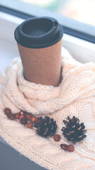 A cup for coffee near the window, a knitted scarf, pine cones, a letter. Autumn and winter background.
