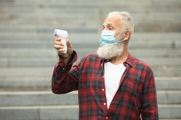 Bearded senior man in face mask holding infrared thermometer a healthy senior man's normal body...