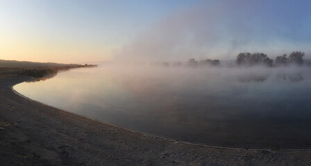 Fog on a calm river in the early morning. Soft sunlight. Focus on the foreground.