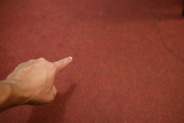 Ein Mann zeigt mit dem Zeigefinger auf den roten Boden. Zu sehen ist nur die linke Hand.