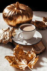 Autumn composition of shiny gold Pumpkin, maple leafes and cup of hot chocolate. Halloween decorations. trendy holiday concept. Golden autumn card.