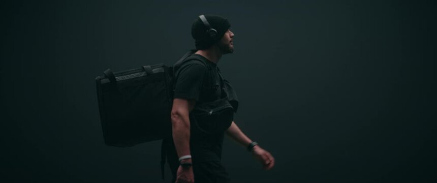 Caucasian male courier walking with a delivery backpack against black background. Shot on RED cinema camera