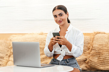 Self employed woman working with her phone and laptop in a cafe with a cup of coffee
