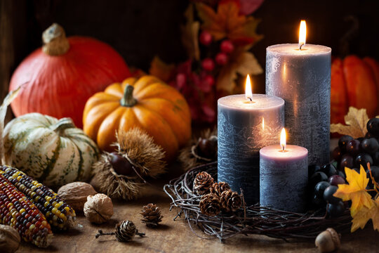 Autumn Or Fall Harvest Concept With Lit Candles, Decorative Pumpkins, Corn, Nuts, Grapes And Pinecones