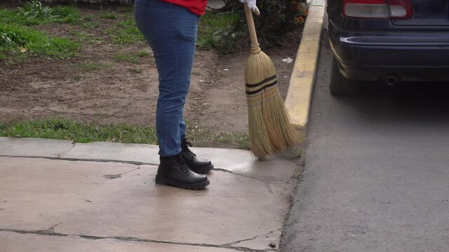 closeup of a girl with gloves cleaning the street with a straw broom with wooden magician