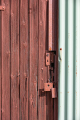 An old door with weathered planks and a broken lock, all painted in red brown beside light green painted metal wall elements