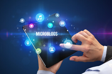 Businessman holding a foldable smartphone with MICROBLOGS inscription, social media concept