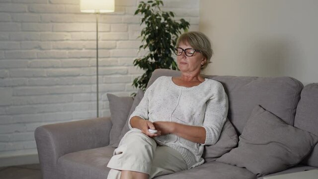 Beautiful Middle Aged Woman Sitting On The Couch In Her Apartment. Something Surprises Her Greatly.