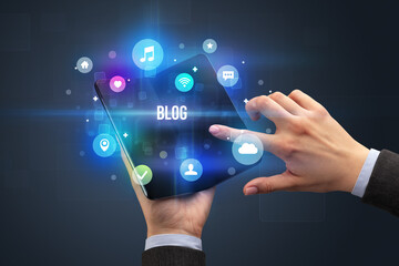 Businessman holding a foldable smartphone with BLOG inscription, social media concept