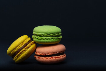 Macaroni, red, yellow, green, are stacked one on top of the other in the form of a tower on a black background. Side view
